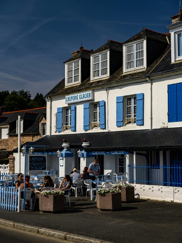 Quaint French creperie with blue shutters and outdoor dining area on a sunny day.